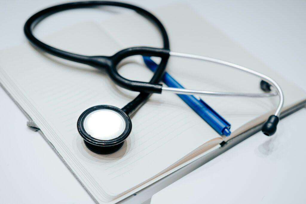 Stethoscope resting on an open notebook beside a blue pen on a clean white surface, symbolizing medical notes or healthcare documentation.