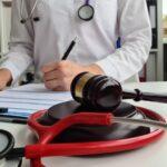 A doctor in a white coat writes on a clipboard while wearing a stethoscope around their neck.